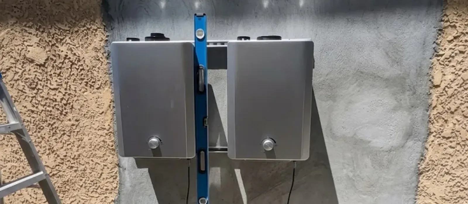 Two tankless water heaters mounted level on an exterior stucco wall